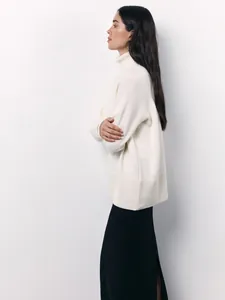 Detail view of a loose cream-colored knit turtleneck sweater with ribbed cuffs and hem.