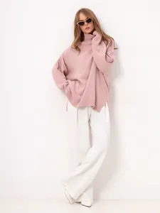 Full body view of a woman wearing a pink high neck knit sweater and white trousers