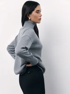 Side view of a woman wearing a grey loose high-neck knitted sweater for winter fashion