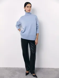 Professional model wearing a light blue loose turtleneck sweater and black leather trousers.