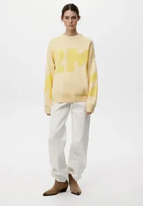 Modell trägt gelben Oversized-Rundhalspullover mit großem 2M-Buchstabenmuster