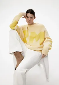 Stylisches Model in blassgelbem Oversize-Strickpullover mit Buchstaben und weißer Hose