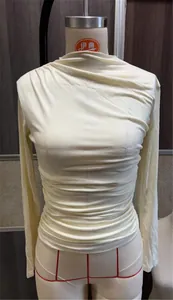 Detalle de camiseta crema de manga larga con elegante diseño fruncido en maniquí