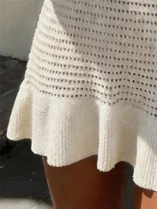 Close-up detail of a white knitted mini dress featuring a feminine ruffled hemline.