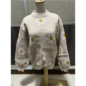 Vue détaillée du motif de marguerite blanche sur un pull en maille beige à col rond