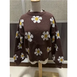 Vue détaillée d'un pull en maille avec des motifs de marguerites sur un fond marron.