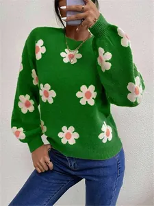 Gros plan d'un pull en tricot vert avec des motifs de fleurs blanches et roses vifs.