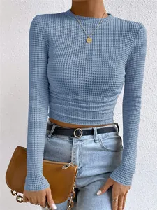 Detail van een slim-fit blauwe wafelgebreide top met lange mouwen en geplooide taille