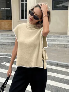 Detailansicht einer beigen ärmellosen Strickweste mit weißem Rand und Seitenschleife.