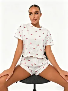 Detail of a white 100% cotton pajama set featuring red cherry prints and ruffled edges