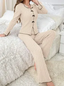 Two-piece beige ribbed pajama set with black piping and bow accents in cozy bedroom setting.