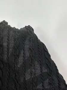 Vista dettagliata della trama a trecce nera e del bordo a lattuga su questo elegante top in maglia.