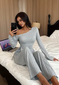 Elegantes Modell in grauem, geripptem, schulterfreiem Loungewear-Set auf einem Bett sitzend