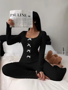 Detail view of cozy black rib-knit pajama set with white bow accents in a bed setting