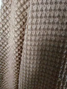 Gros plan détaillé montrant le motif de tricot texturé complexe d'un cardigan champagne