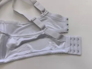 Macro view of white satin bra closure showing adjustable straps and metal hooks.