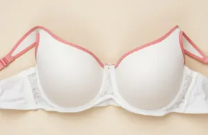 Close-up of a white plus size bra with pink trim and lace detail on a beige background