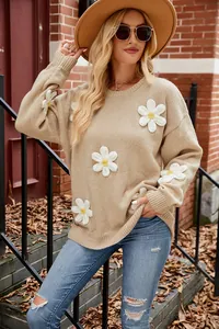 Beige knitted sweater featuring 3D white crochet flower appliqués on a model outdoors