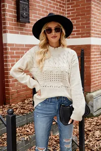 Detailed view of a white cable knit sweater featuring chic pom-pom accents on a model