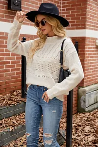 Detail of a cream cable-knit pullover sweater paired with distressed jeans and a hat.