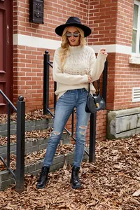 Chic cream cable knit sweater styled with ripped jeans and a black hat for autumn