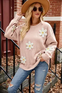 Close-up of pink knit sweater featuring white 3D crochet flowers in outdoor setting
