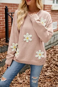 Detail view of a pink loose knit sweater featuring unique 3D white crochet flower appliques.