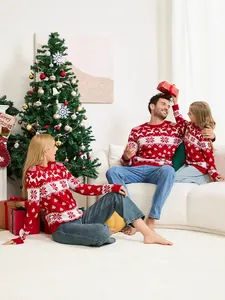 Family wearing matching red Christmas sweaters with reindeer and snowflake patterns in cozy home.