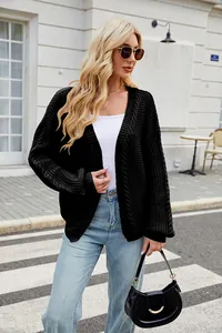 Detail shot of a black cable-knit cardigan sweater on a model in a street setting.