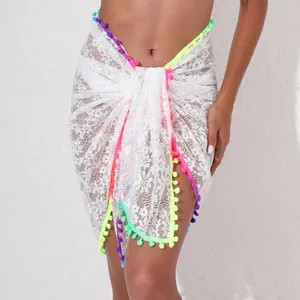 Detail of white lace beach sarong with colorful pom-pom trim and floral see-through pattern
