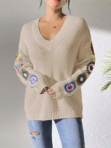 Detail showing colorful crochet flower patchwork on beige V-neck knit sweater sleeves.