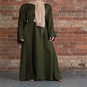 Loose plus size dark green maxi dress with belt on a model against a brick wall