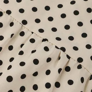 Macro view showing the fabric texture and black polka dot pattern of the cream dress.