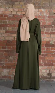Back view of a modest dark olive green abaya dress with beige hijab against brick wall