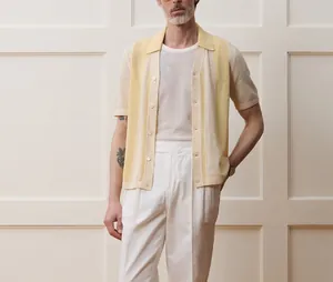 Close-up of a men's yellow striped open-knit polo shirt paired with white trousers.