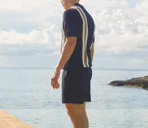 Side view of a men's navy knit Polo shirt with white and tan stripes by the pool