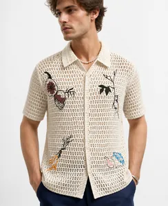 Detail view of men's cream crochet knit shirt with colorful vegetable embroidery.