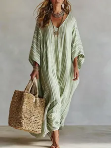 Detail of a bohemian striped kaftan dress with V-neckline and straw bag accessory