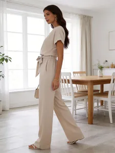 Side view of woman wearing elegant beige short sleeve wide-leg jumpsuit in a bright room