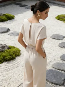 Back view of a chic beige linen jumpsuit with wide-leg pants in a Zen garden setting.