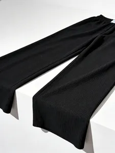 Macro detail of black pleated fabric on high-waist wide-leg trousers with loose fit