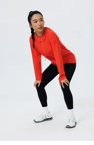 Vue complète d'une femme portant un coupe-vent de course à capuche orange vif et un legging.