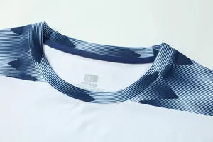 Detailopname van de ronde hals van een ademend wit en marineblauw voetbalshirt