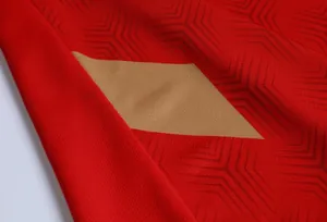 Primo piano del tessuto traspirante della maglia da calcio rossa con dettaglio oro.
