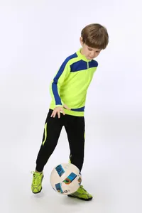 Jungen-Modell in neongrüner Fußball-Trainingsjacke und schwarzer Hose spielt mit Fußball