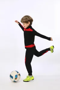 Kind im schwarz-roten Fußball-Trainingsanzug beim Ballkicken im professionellen Studio