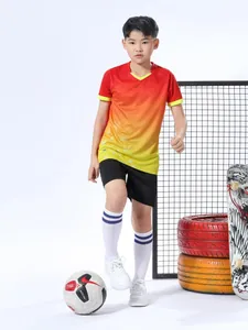 Ganzkörperansicht eines Jungen in einem rot-gelben Fußballtrikot-Trainingsset mit Farbverlauf