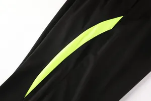 Detailansicht des schwarzen Fußball-Trainingsjackenstoffs mit neongelbem Streifen-Detail.