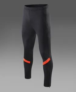 Détail d'un pantalon de football noir avec bandes orange et zips aux chevilles.