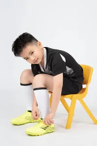 Detailansicht eines schwarzen Kinder-Fußballtrikots an einem Jungen mit gelben Schuhen